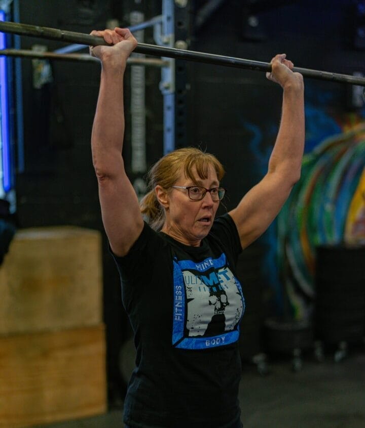 Woman learning to press a barbell overhead.